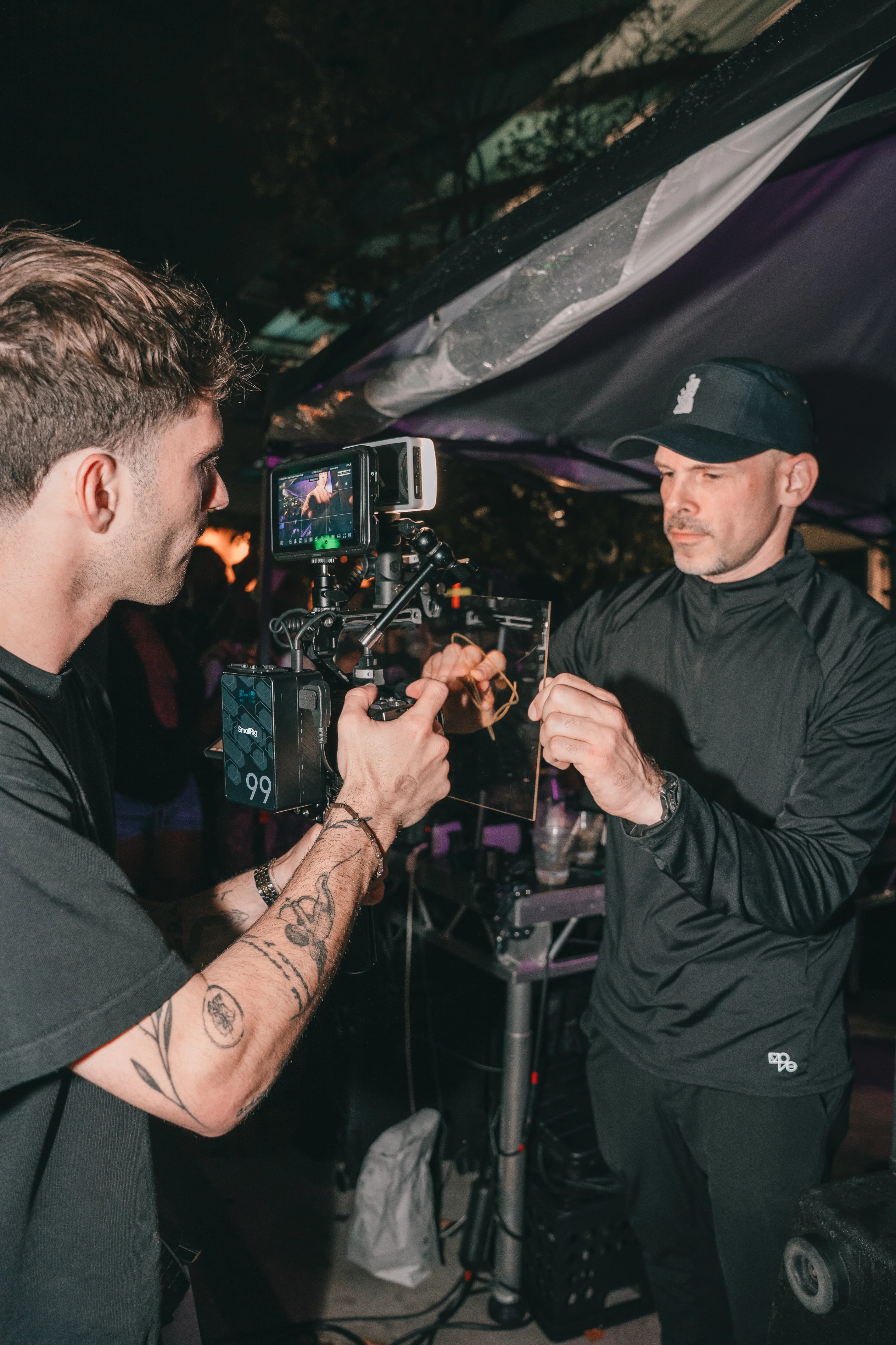 A Blank videographer operates a rigged cinema camera during a night shoot at Dante's HiFi+, filming a man in a cap holding up a glass filter.