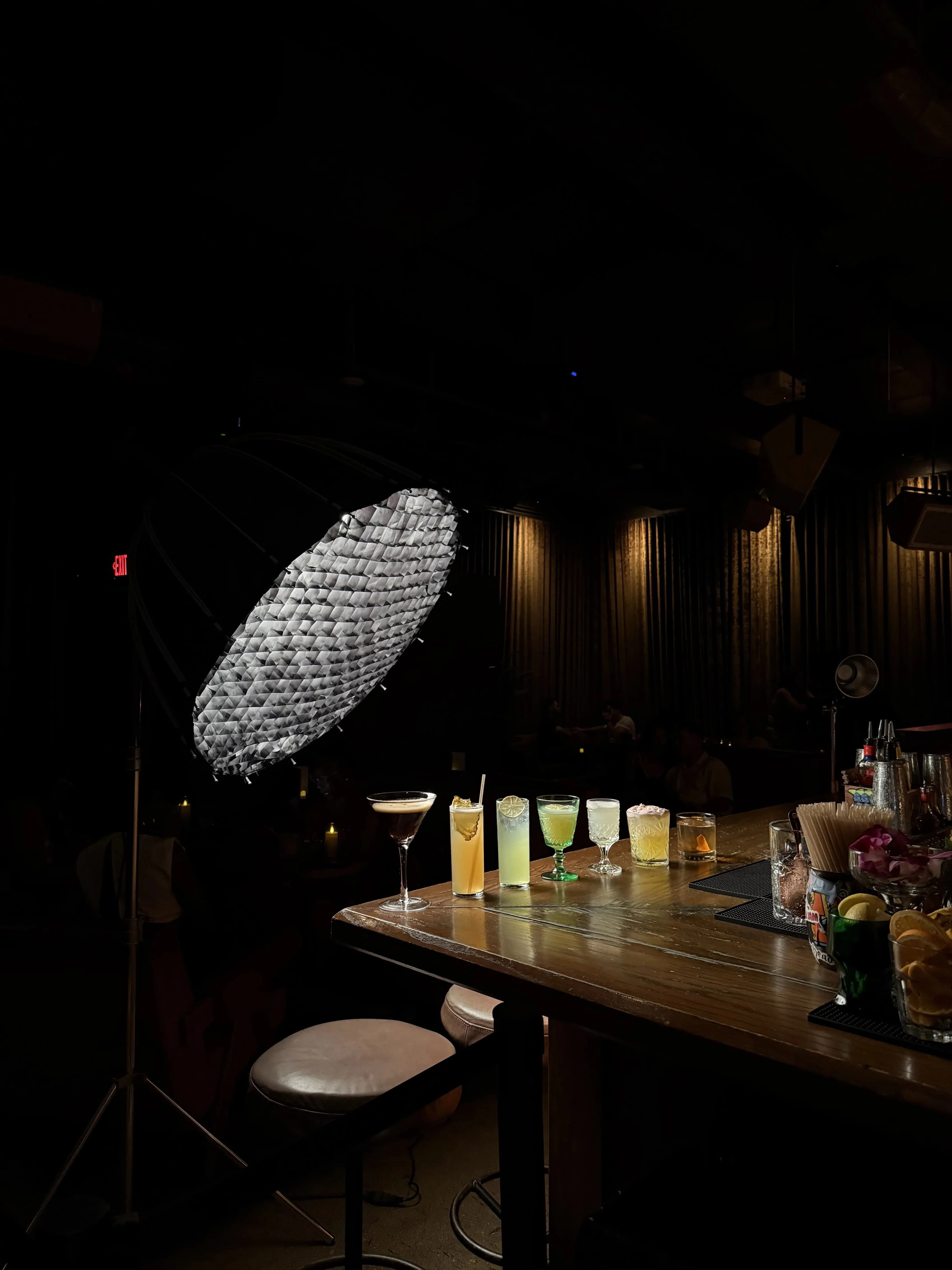 A large parabolic softbox on a stand lights a lineup of cocktails along the bar during a behind-the-scenes shoot at Dante's HiFi+.