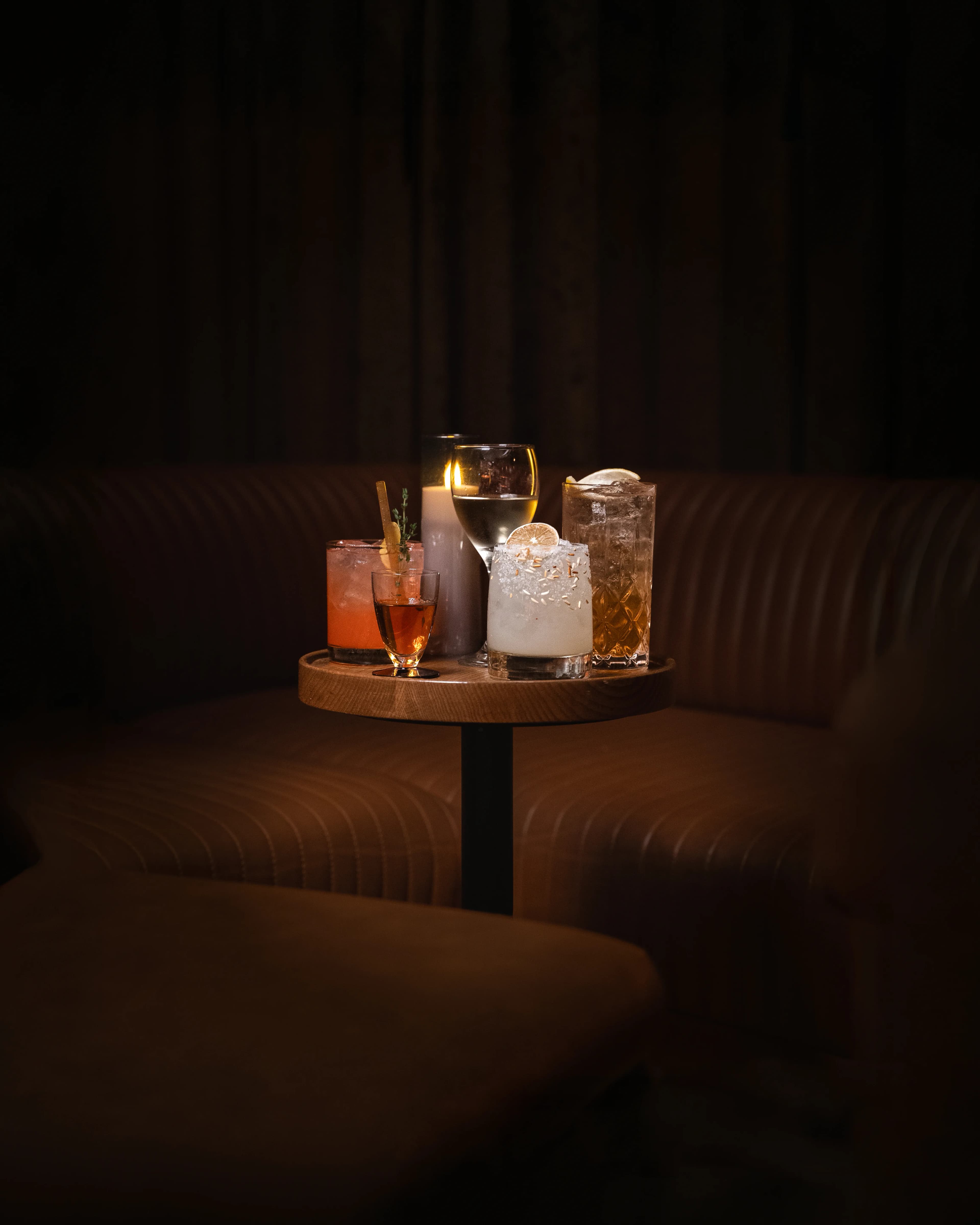 Cocktails and a lit candle arranged on a small round table in the dim, warm-lit lounge at Dante's HiFi+.