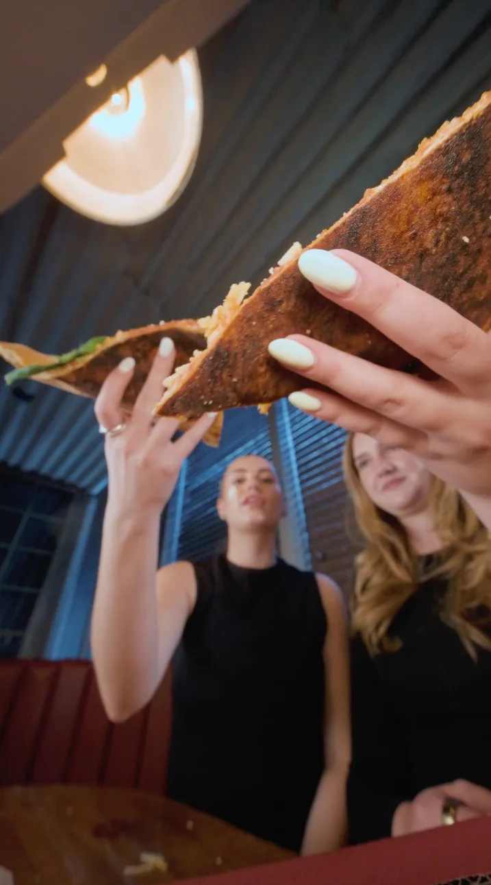 Two guests hold up a folded slice beneath warm lights at DC Pie Co.
