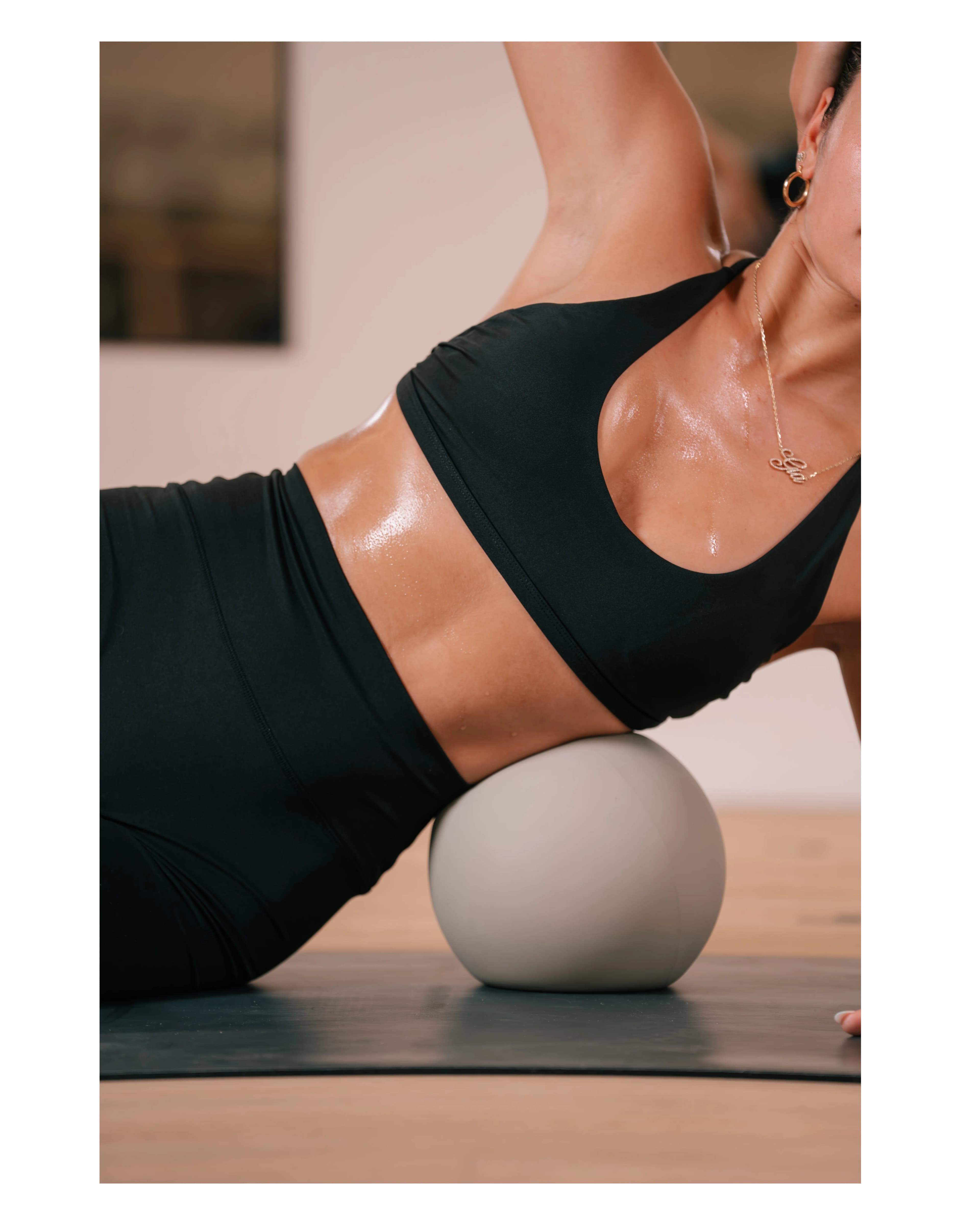 A woman in black activewear balances over a small pilates ball on the mat at Pure Motion.