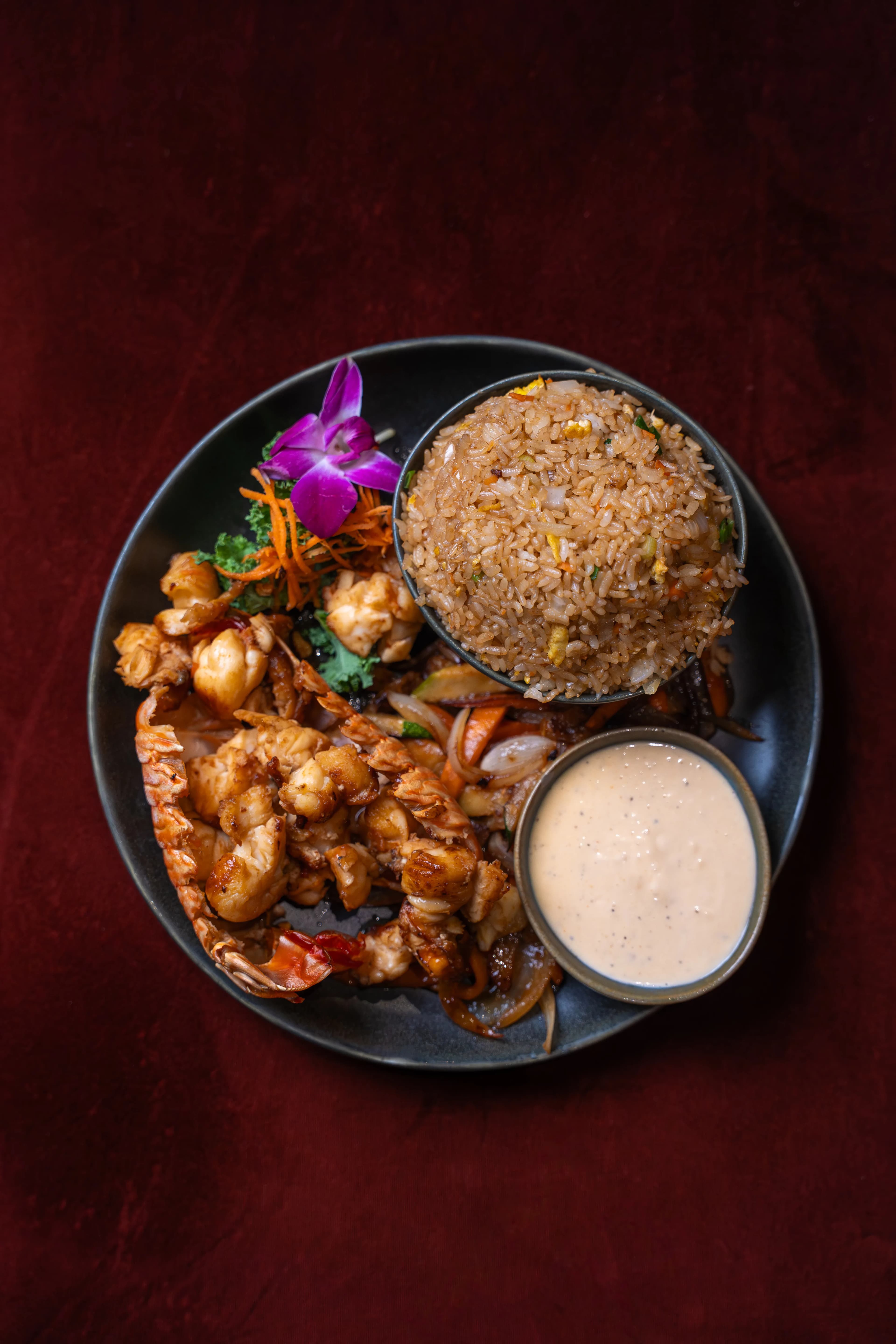 An overhead flat-lay of Sushi Sake's lobster fried rice — fried rice, wok-tossed lobster, and house sauce on a dark plate over red velvet.