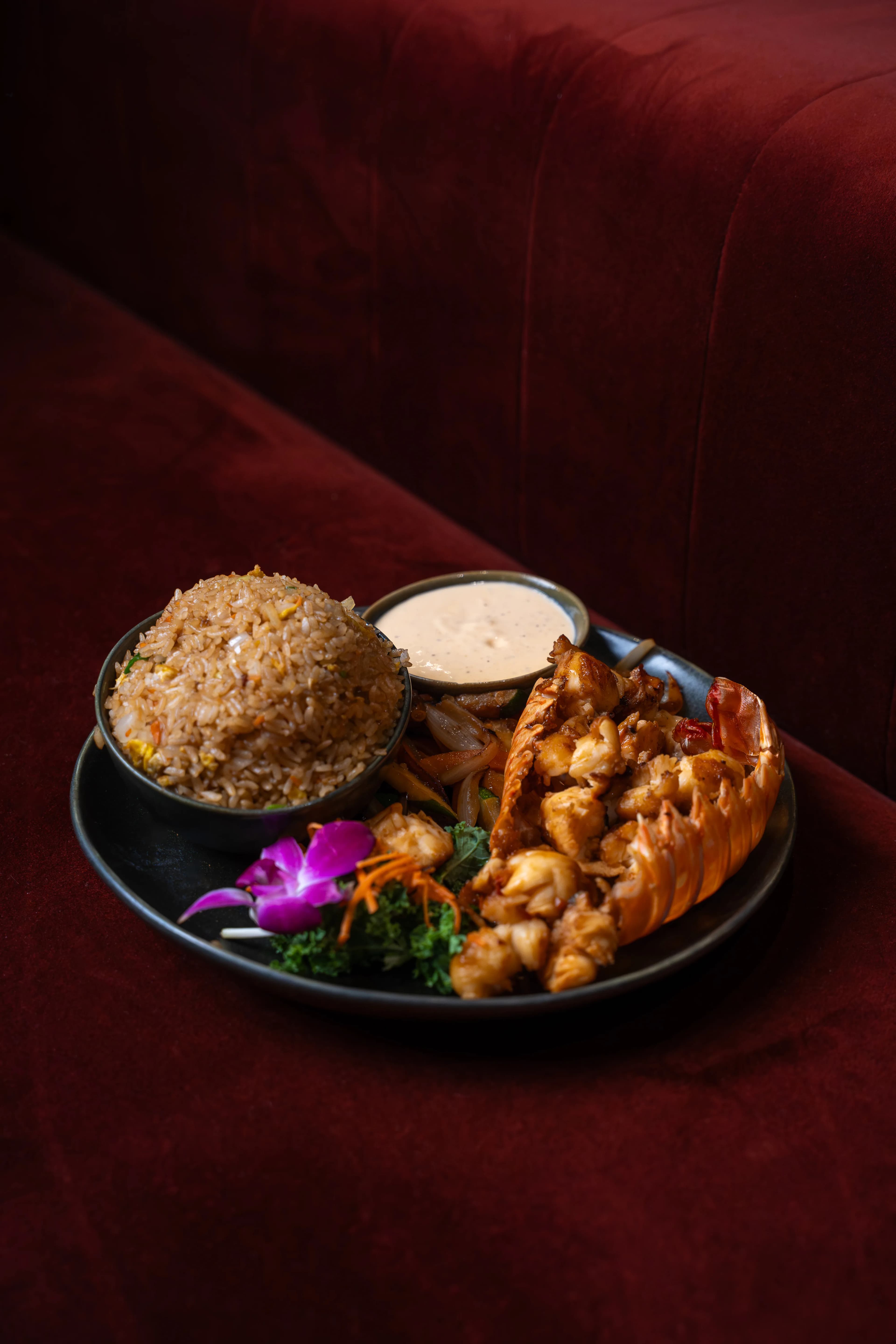 An angled view of Sushi Sake's lobster fried rice plate on a red velvet booth — fried rice, lobster, and house sauce.