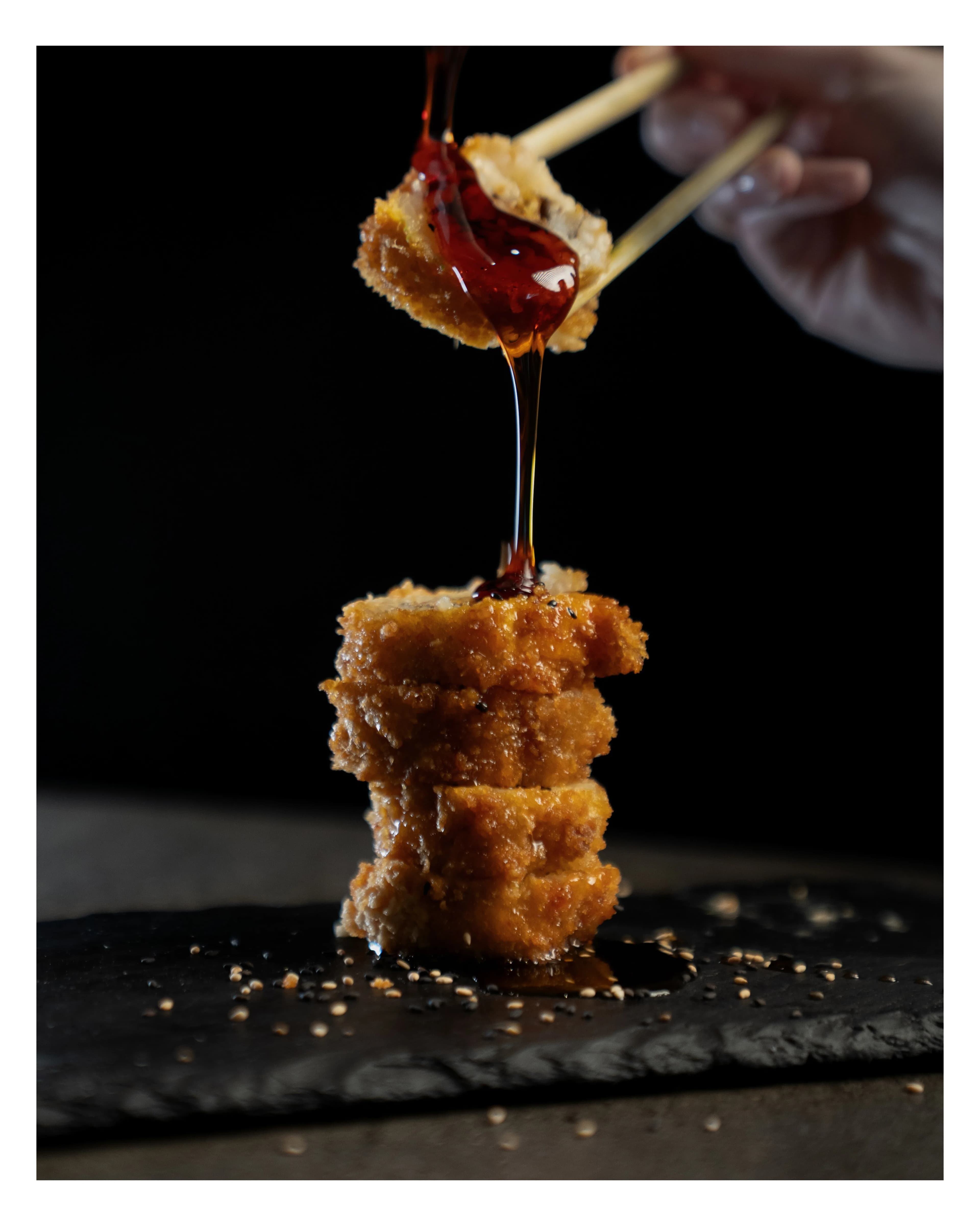 Chopsticks lift a sauced crispy-rice cube from a stack at Sushi Sake.