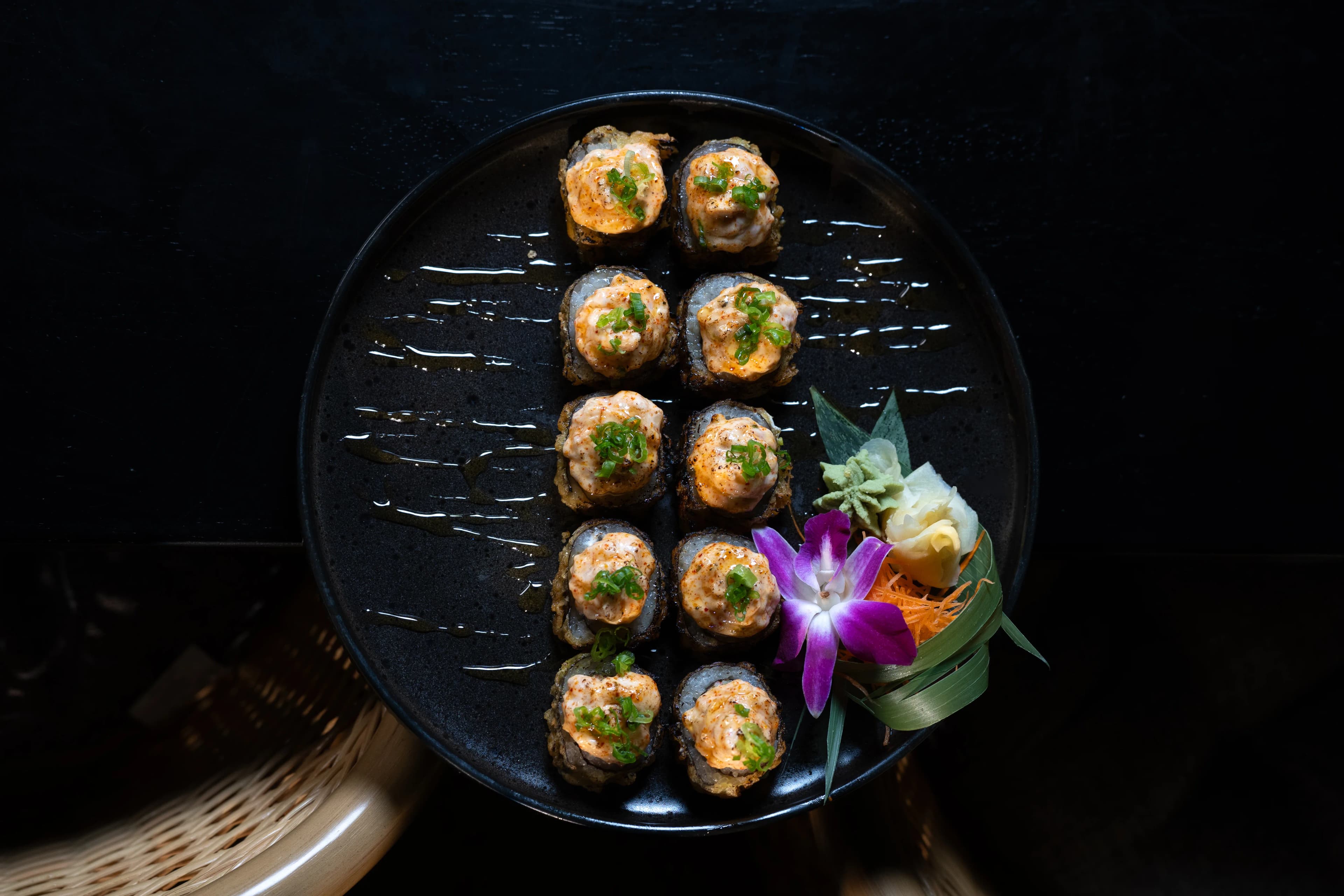 An overhead plate of sushi rolls garnished with an orchid on a dark table at Sushi Sake.