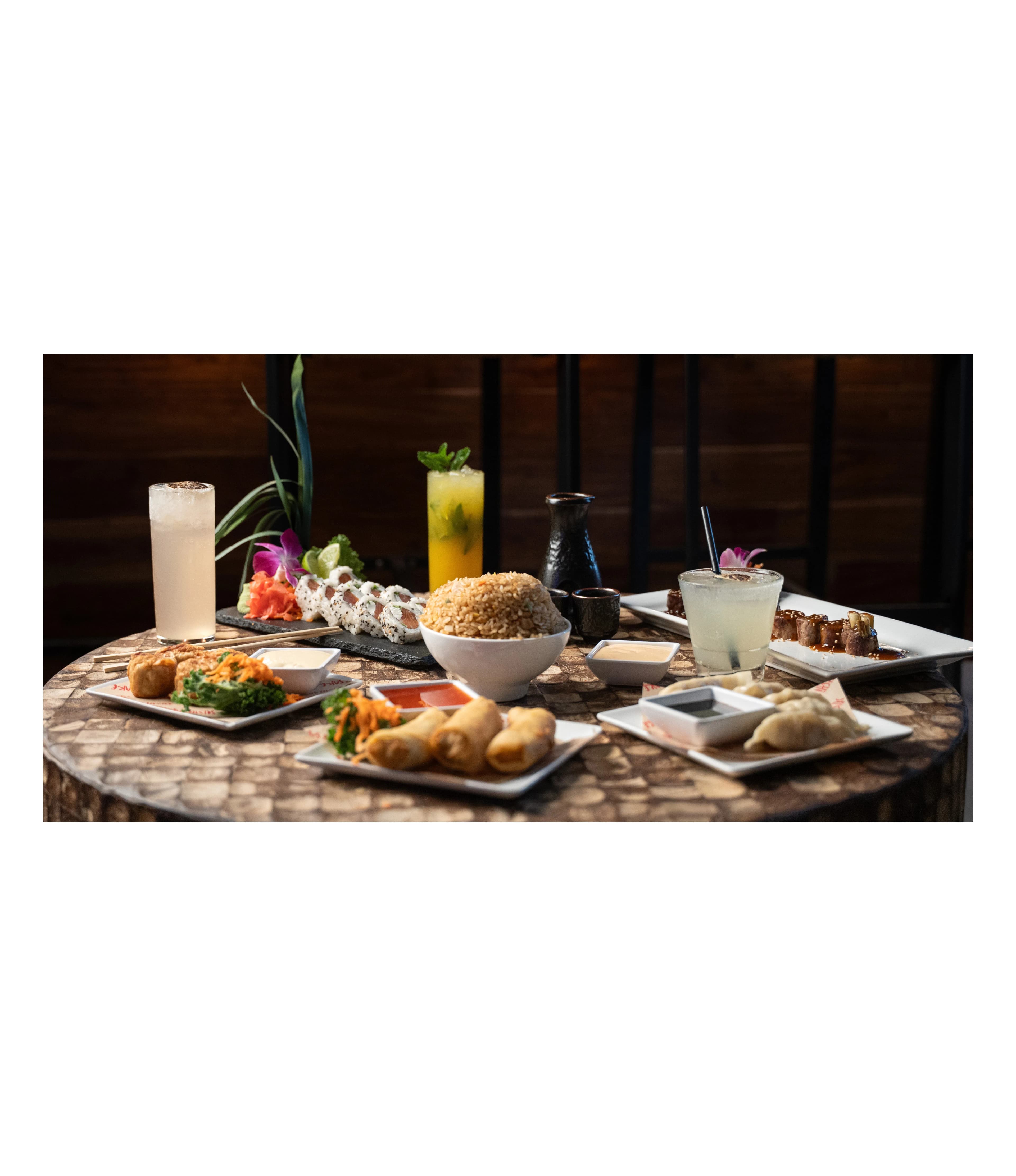 A rustic table spread of Sushi Sake dishes and drinks under warm light.