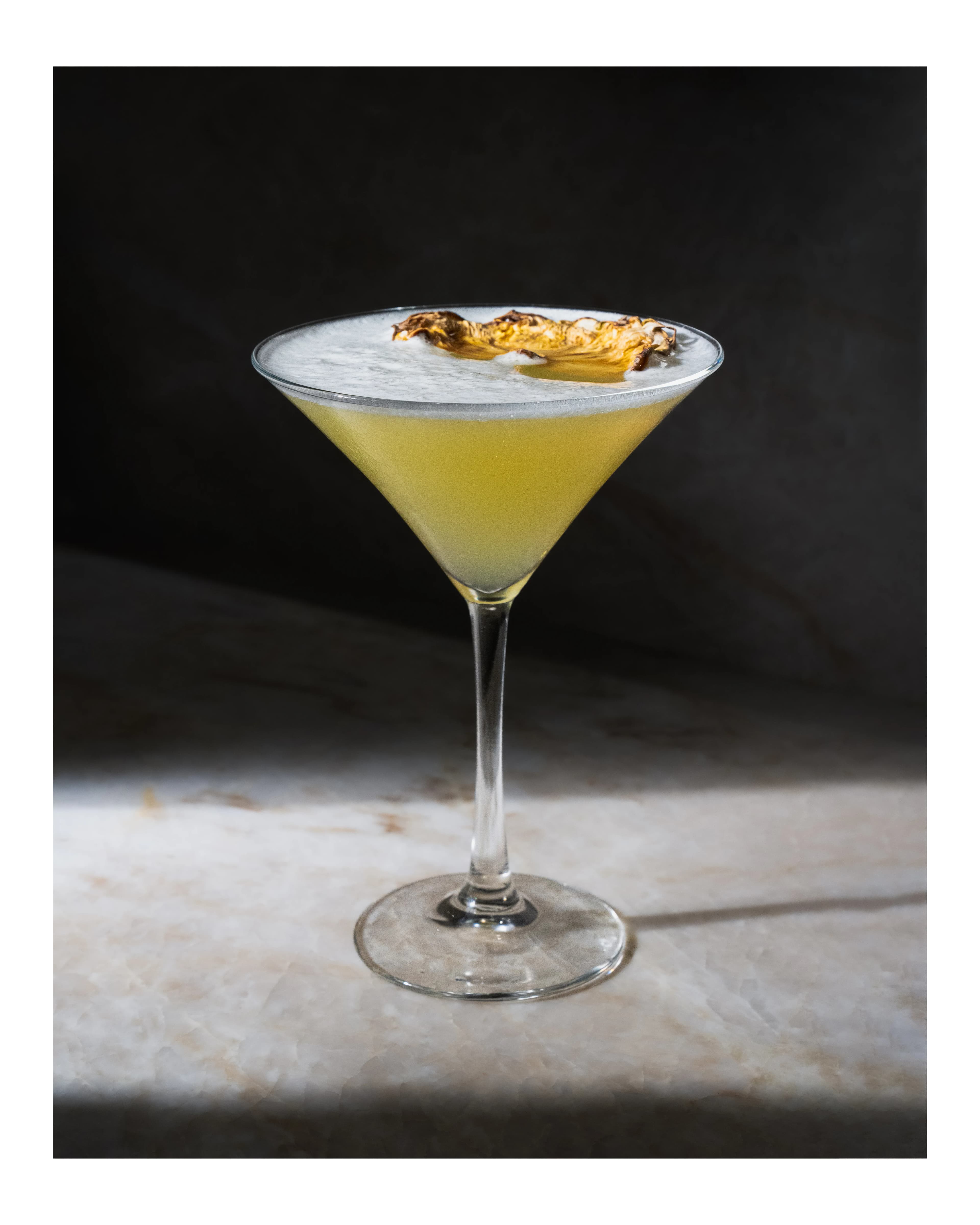 A citrus-yellow cocktail crowned with gold leaf against a grey backdrop at Sushi Sake.