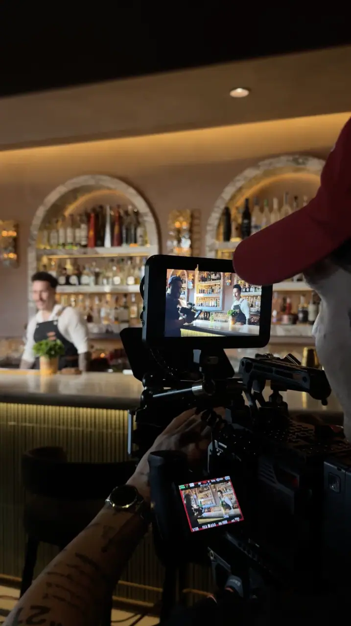 Behind the scenes — videographer filming a bartender behind a lit back bar.